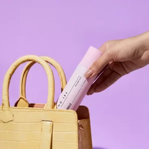 Déodorant 384 pour femme de Bargello inspiré de Bombshell, présenté à la main avec un sac à main beige sur un fond lilas féminin et élégant.
